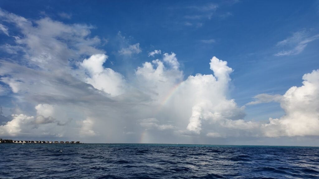 海の上から見たホテルの水上ヴィラと、雲の間にかかる虹